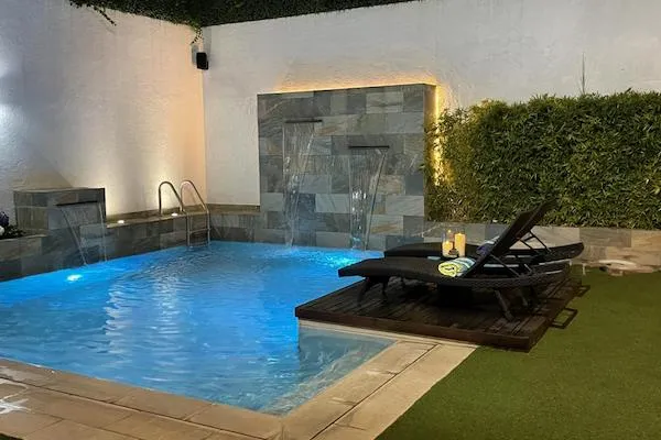 Alberca residencial con cascada y muro de piedra iluminado por Pool Designers